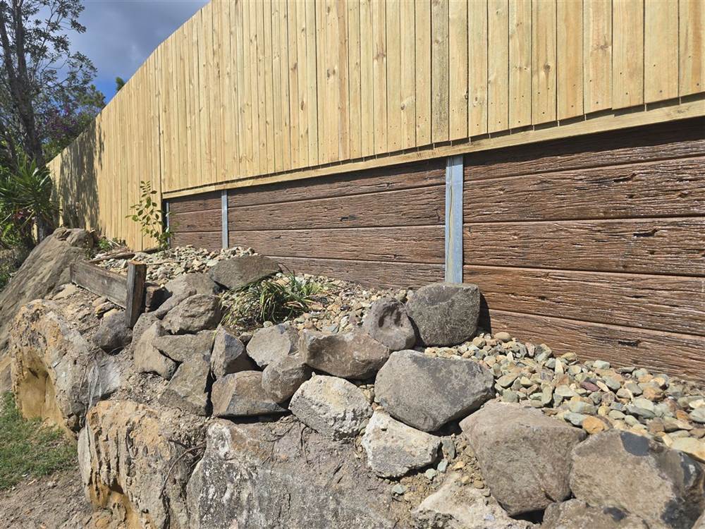 Timber-look concrete sleeper retaining wall with a rock wall and planting below