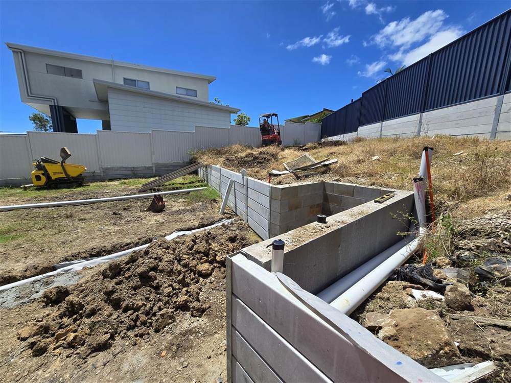 Concrete sleeper retaining walls under construction with ag drain laid before backfill